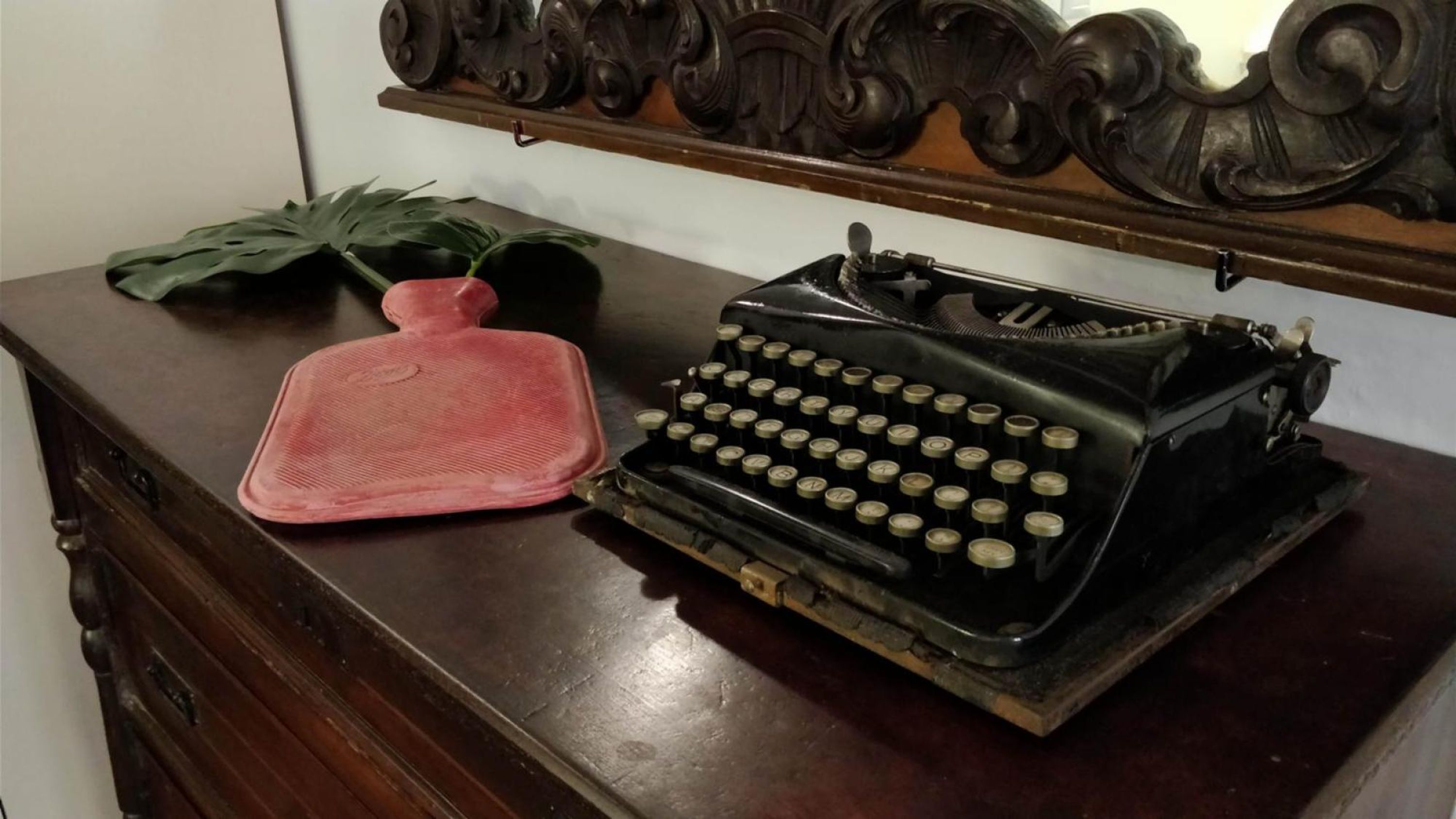 A vintage typewriter on a wooden dresser with a decorative shelf above.