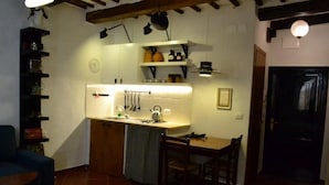 A compact kitchen with a sink, countertop, and hanging utensils. There is a dining table with chairs and a small sofa. - Casa Messi - Casa Messi a Vicolo Della Rivolta 31 Apt 2 (Pitigliano)