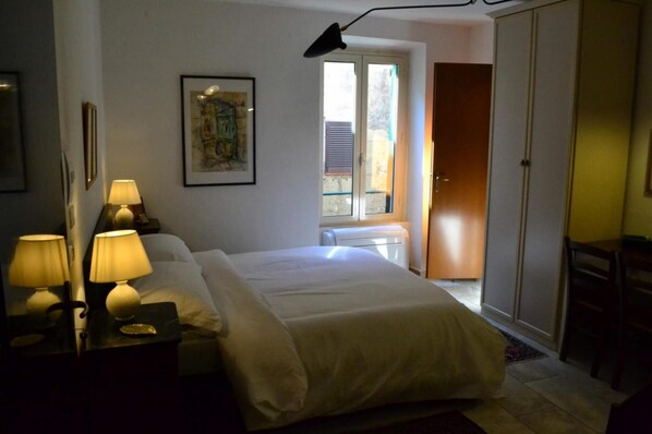 Une chambre à coucher comprenant un lit, des lampes de chevet, un tableau encadré, une fenêtre et une armoire.