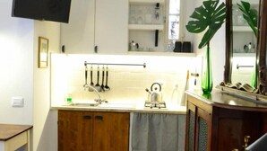 A compact kitchen with a sink, cabinets, and a small countertop. There is a chair and a television mounted on the wall. - Casa Messi - Casa Messi a Vicolo Della Rivolta 31 Apt 3 (Pitigliano)