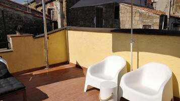 Une terrasse sur le toit avec deux chaises en plastique blanches, un petit tabouret blanc et un grand parasol noir.