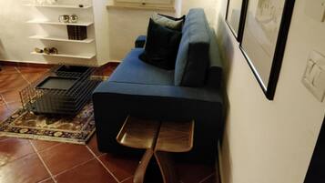 A living room with a dark blue sofa, a wooden bench, a TV, a window, and a tiled floor.