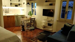 A compact living space with a kitchenette, a dining area, a TV mounted on the wall, and a sofa. - Casa Messi - Casa Messi a Vicolo Della Rivolta 31 Apt 4 (Pitigliano)