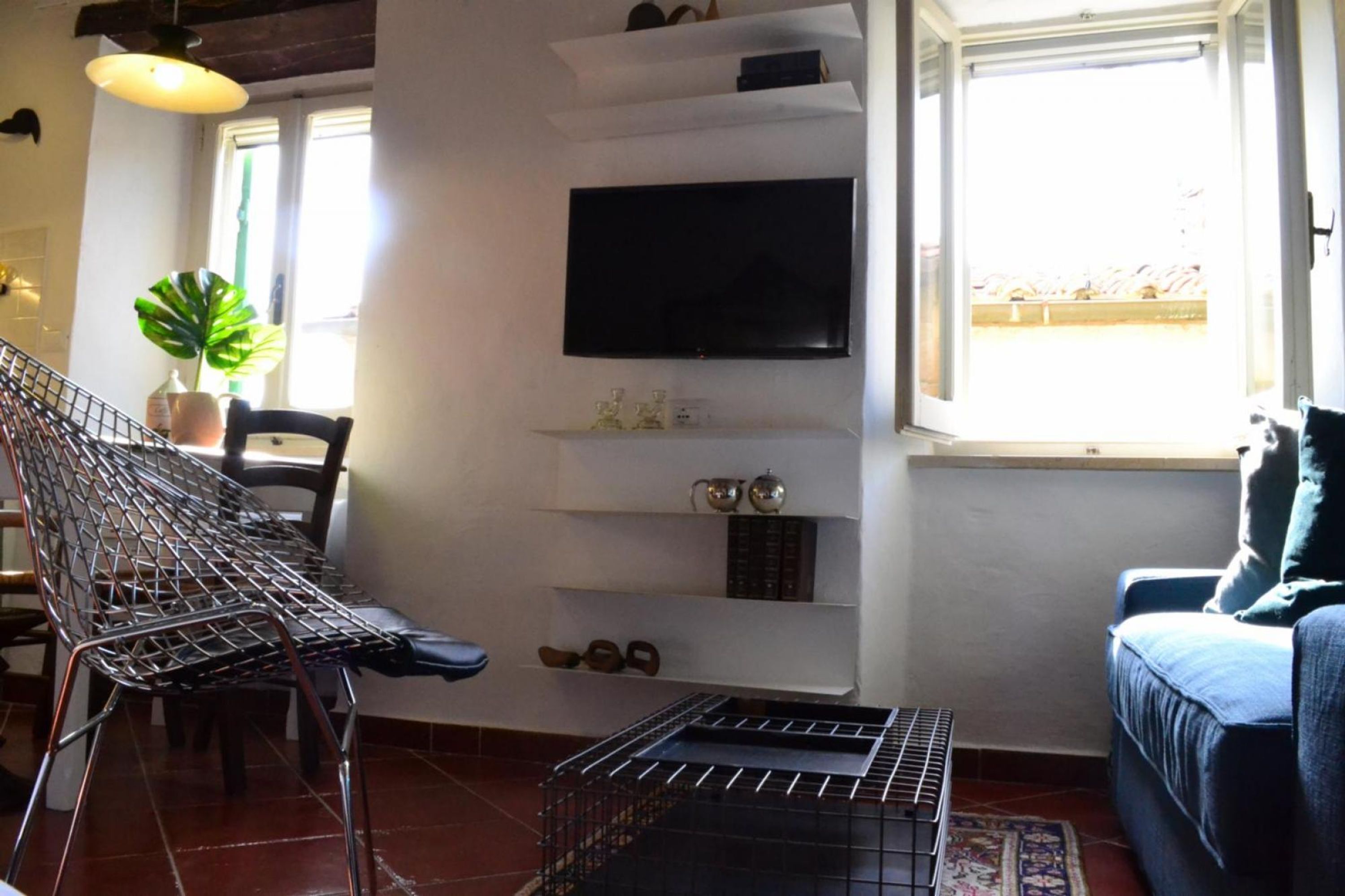 Una sala de estar con televisión instalada en la pared, una butaca, un sofá y una mesita.