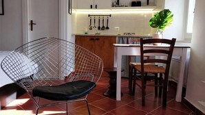 A modern kitchen with white cabinets, a hanging pot rack, and a dining area with a wire chair and a wooden dining chair. - Casa Messi - Casa Messi a Vicolo Della Rivolta 31 Apt 4 (Pitigliano)