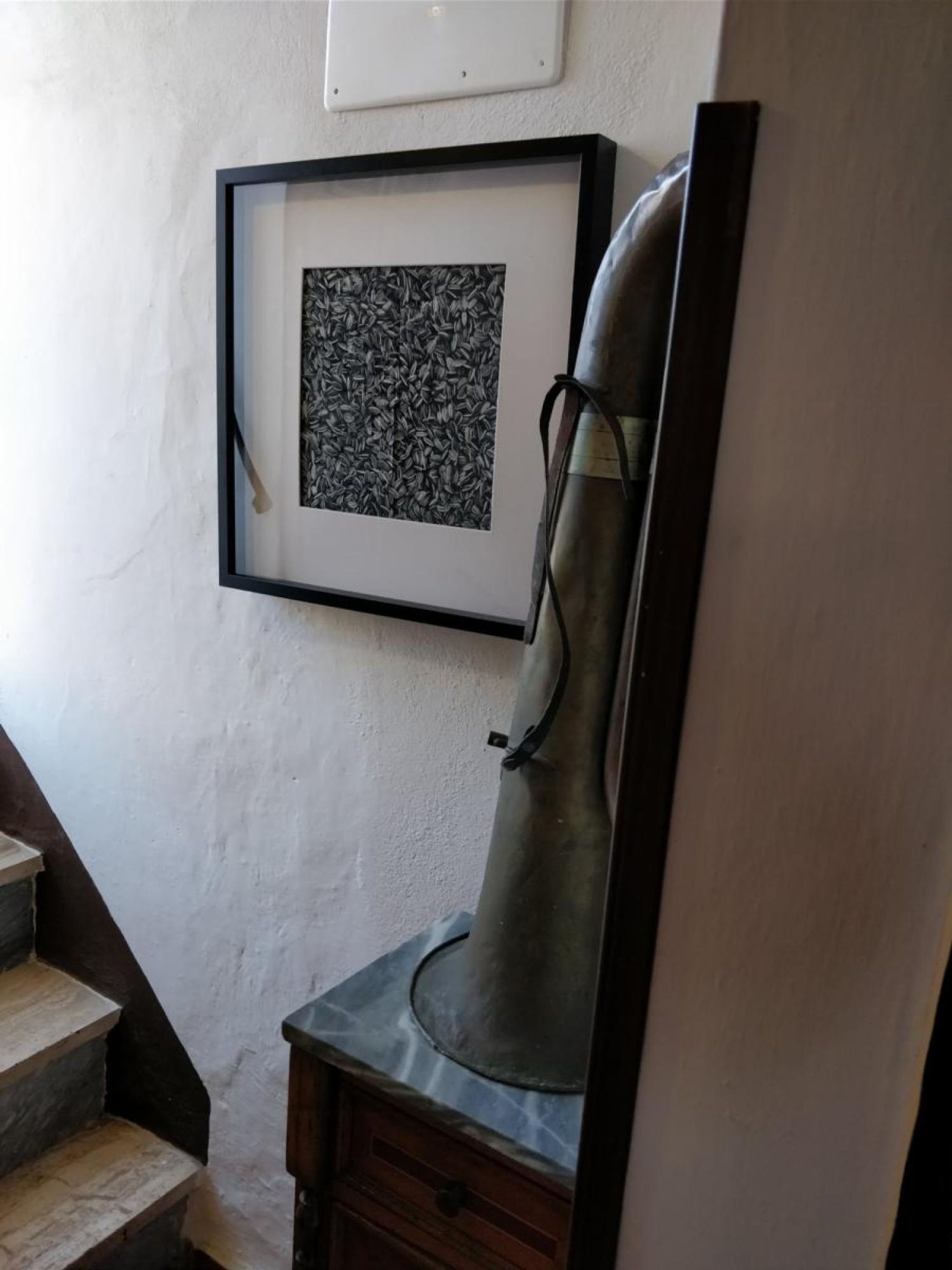 Una obra de arte en un marco en la pared, una silla de metal y una escalera.