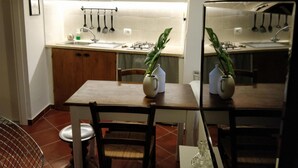 A modern kitchen with white cabinets, a wooden dining table, and a hanging plant. - Casa Messi - Casa Messi a Vicolo Della Rivolta 31 Apt 4 (Pitigliano)