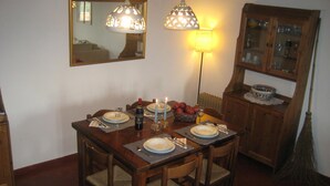 Un coin repas avec une table en bois dressée pour quatre personnes, deux lampes suspendues, un miroir et un buffet aux portes vitrées.