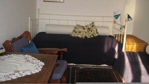 Une chambre à coucher avec un lit, des lampes de chevet, une table en bois recouverte d’une nappe en dentelle et un panier en osier.