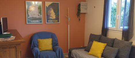 A living room with a sofa, armchair, dining table, and posters on the wall.
