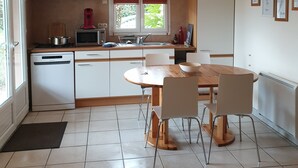 Une cuisine moderne avec des meubles blancs, une table à manger avec des chaises, un four encastré et un luminaire suspendu.
