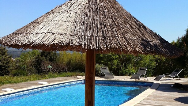 Un espace aménagé au bord de la piscine, avec un parasol en chaume, des chaises longues et une terrasse en bois.