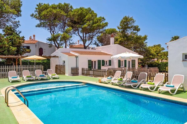 A swimming pool with lounge chairs and a white building with a tiled roof.