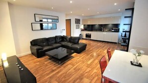 A modern living room with a sectional sofa, a glass coffee table, and a dining area with a white table and red chairs.