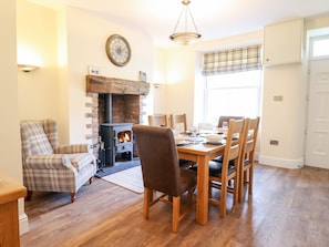 A dining room with a fireplace, wooden dining table, chairs, and a plaid armchair. - Craigside (Betws-Y-Coed)