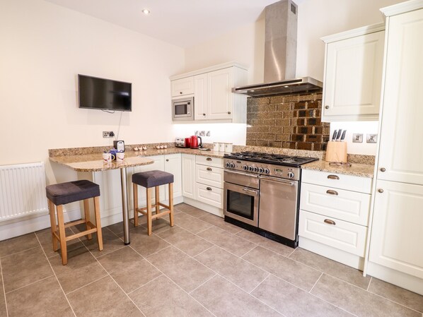 A modern kitchen with white cabinets, a stainless steel stove, and a flat-screen TV mounted above the counter.