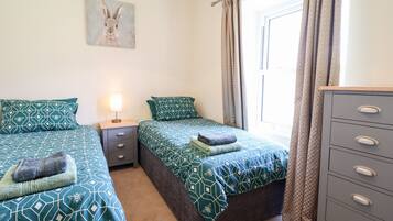 Une chambre avec deux lits, une table de chevet avec une lampe, une commode et une fenêtre avec des rideaux.