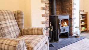 Una sala de estar acogedora con chimenea, un sofá escocés y un estante de madera con libros y una vela.