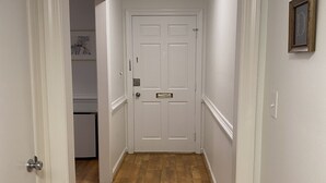 A hallway with a white door at the end, wooden flooring, and a ceiling light.