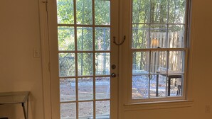 A room with a wooden floor, a white door with glass panels, and a window with a view of a backyard.