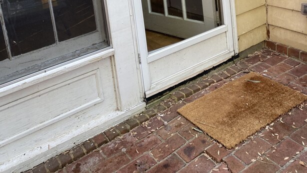 A white door with a glass panel, a brown doormat, and a brick floor.