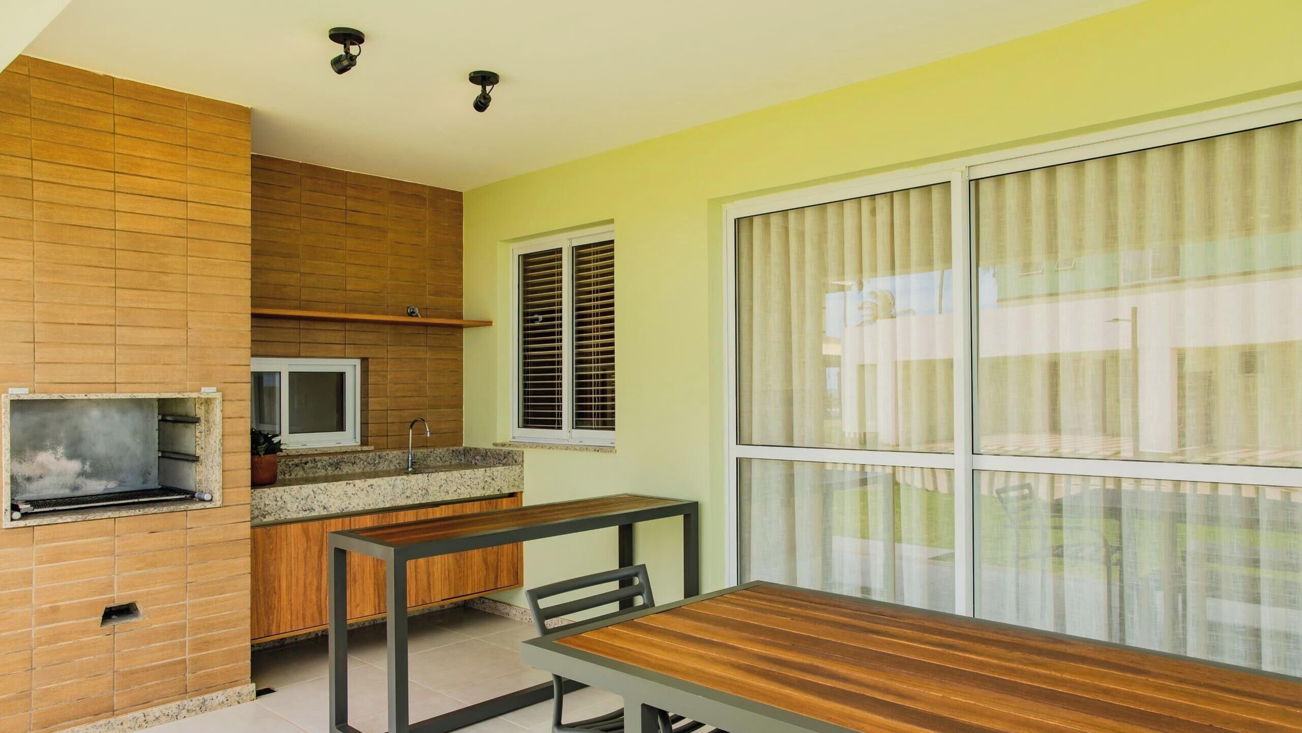 A compact kitchen with a built-in grill, a window with blinds, and a dining area with a table and chairs.