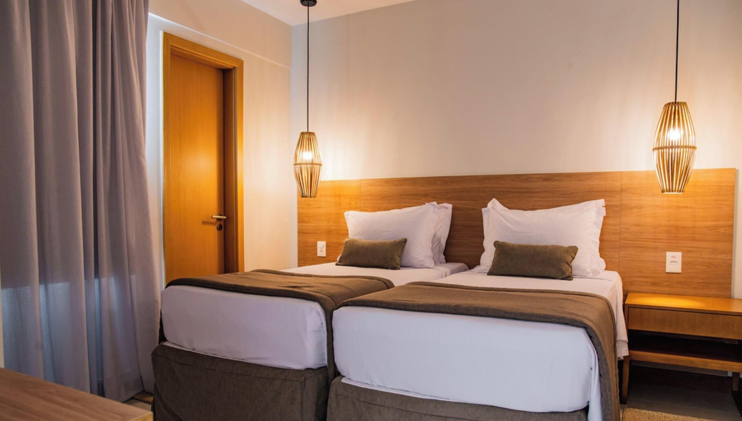 A hotel room with two beds, a wooden headboard, and two pendant lights.