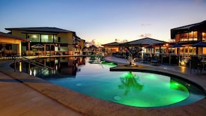 A resort pool area with a clear water feature, surrounded by buildings with outdoor seating. - Ponta de Inhambupe Residences (Esplanada)