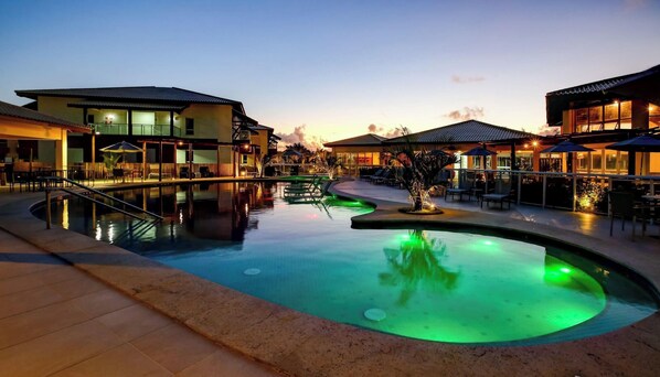 A hotel pool area with a curved pool, lounge chairs, and umbrellas.
