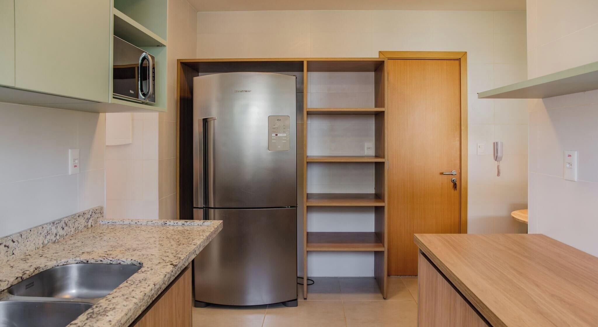 A compact kitchen with a stainless steel refrigerator, a double sink, and wooden cabinets.