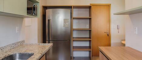 A compact kitchen with a stainless steel refrigerator, a double sink, and wooden cabinets.
