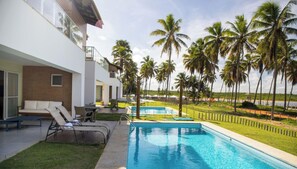 A pool area with lounge chairs and a building with a balcony. - Ponta de Inhambupe Residences (Esplanada)