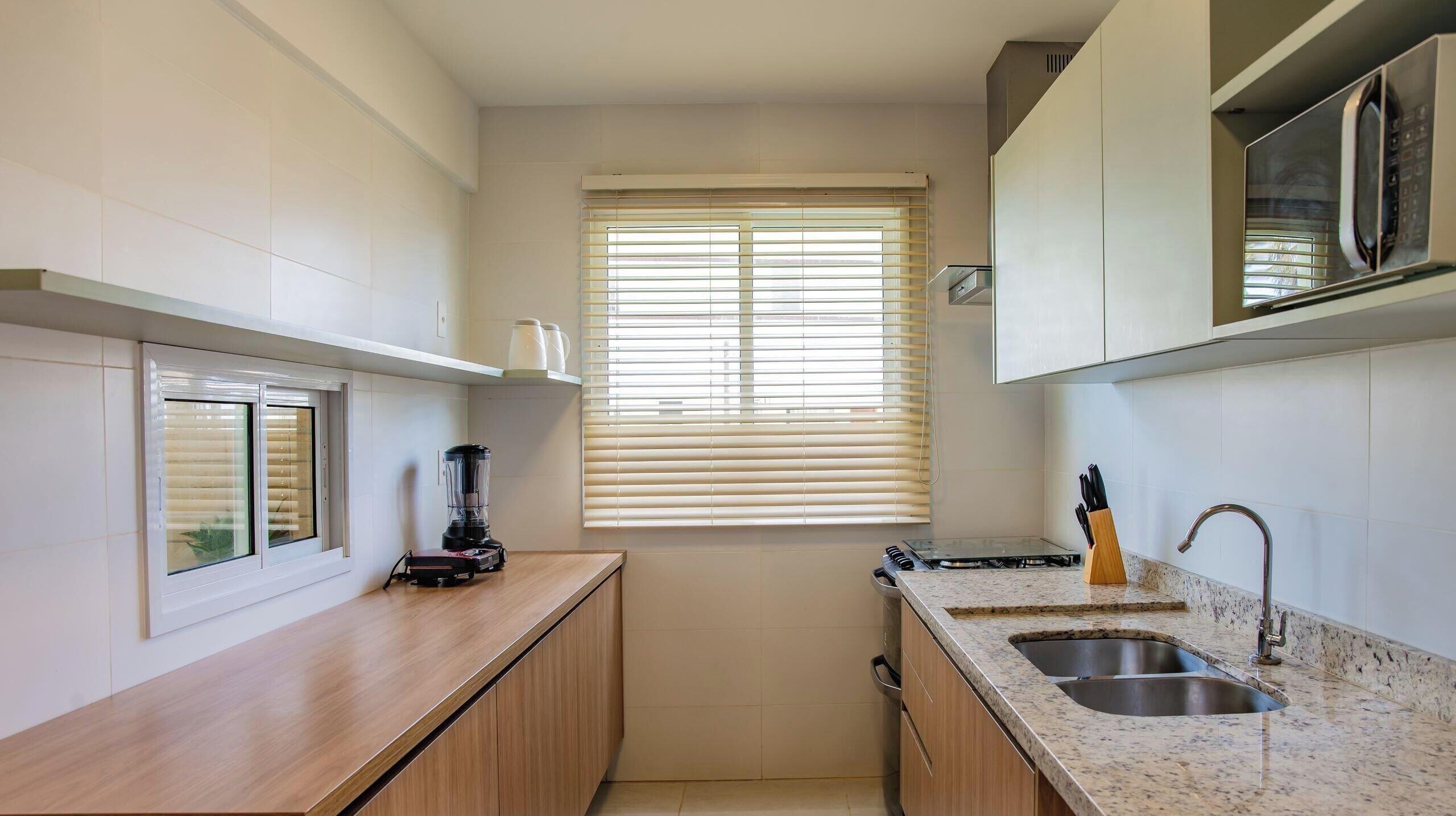 Uma cozinha compacta com micro-ondas embutido, pia e janela com cortinas.