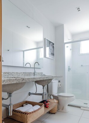 A modern bathroom with a marble sink, a large mirror, a toilet, and a glass shower enclosure.