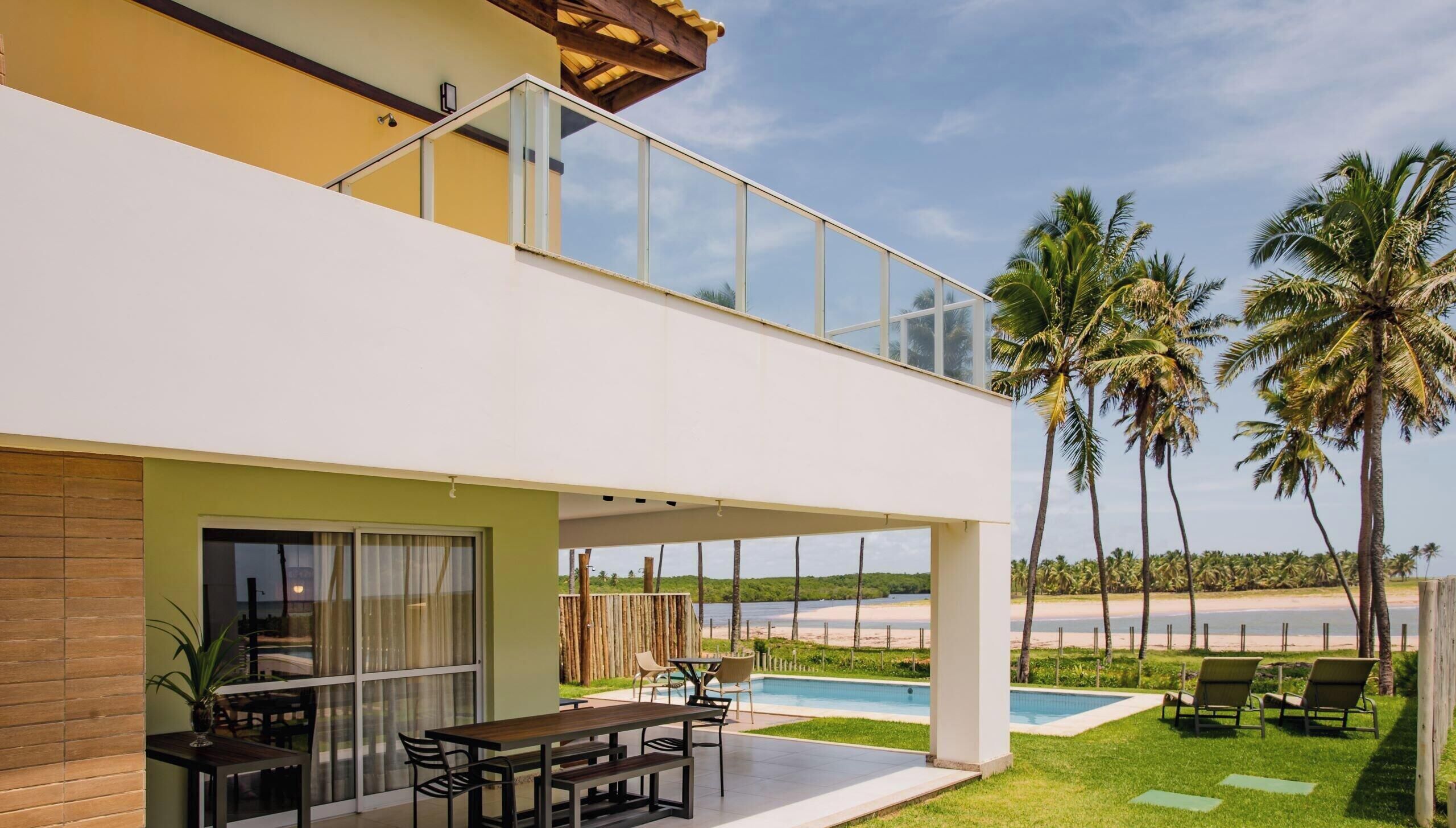 A two-story house with a covered patio, a pool, and a view of the beach.