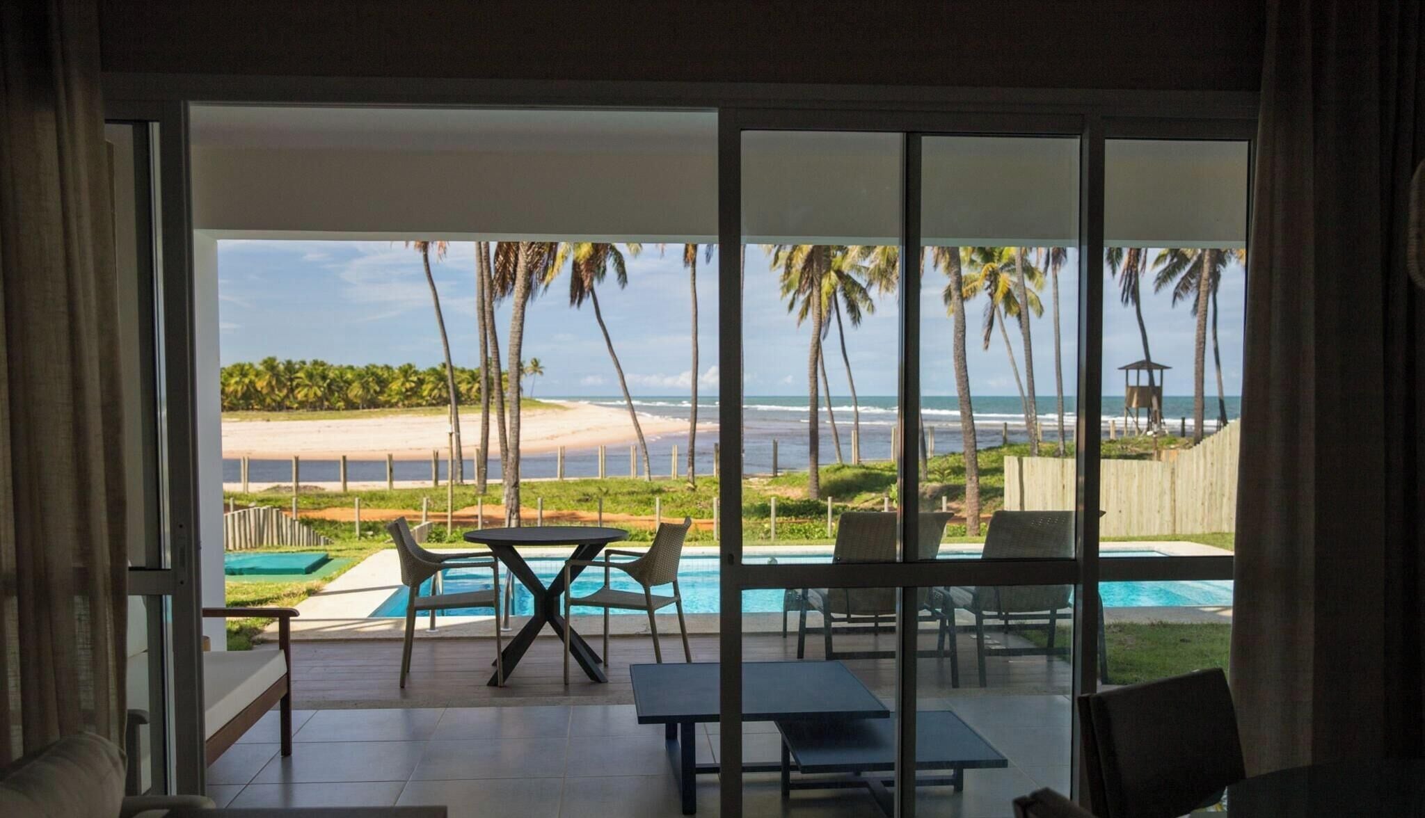 A room with a glass door leading to a pool area with a view of the beach and ocean.