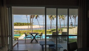 Una habitación con puerta de vidrio que da a una zona de piscina con vista a la playa y al océano.