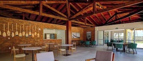 Amplio espacio interior con techos altos y vigas de madera a la vista, con diversas opciones de asiento y una pared de ladrillo donde se exhiben tablas de remo.