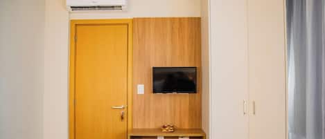 Una habitación con puerta de madera, televisor montado y una pequeña estantería de madera.