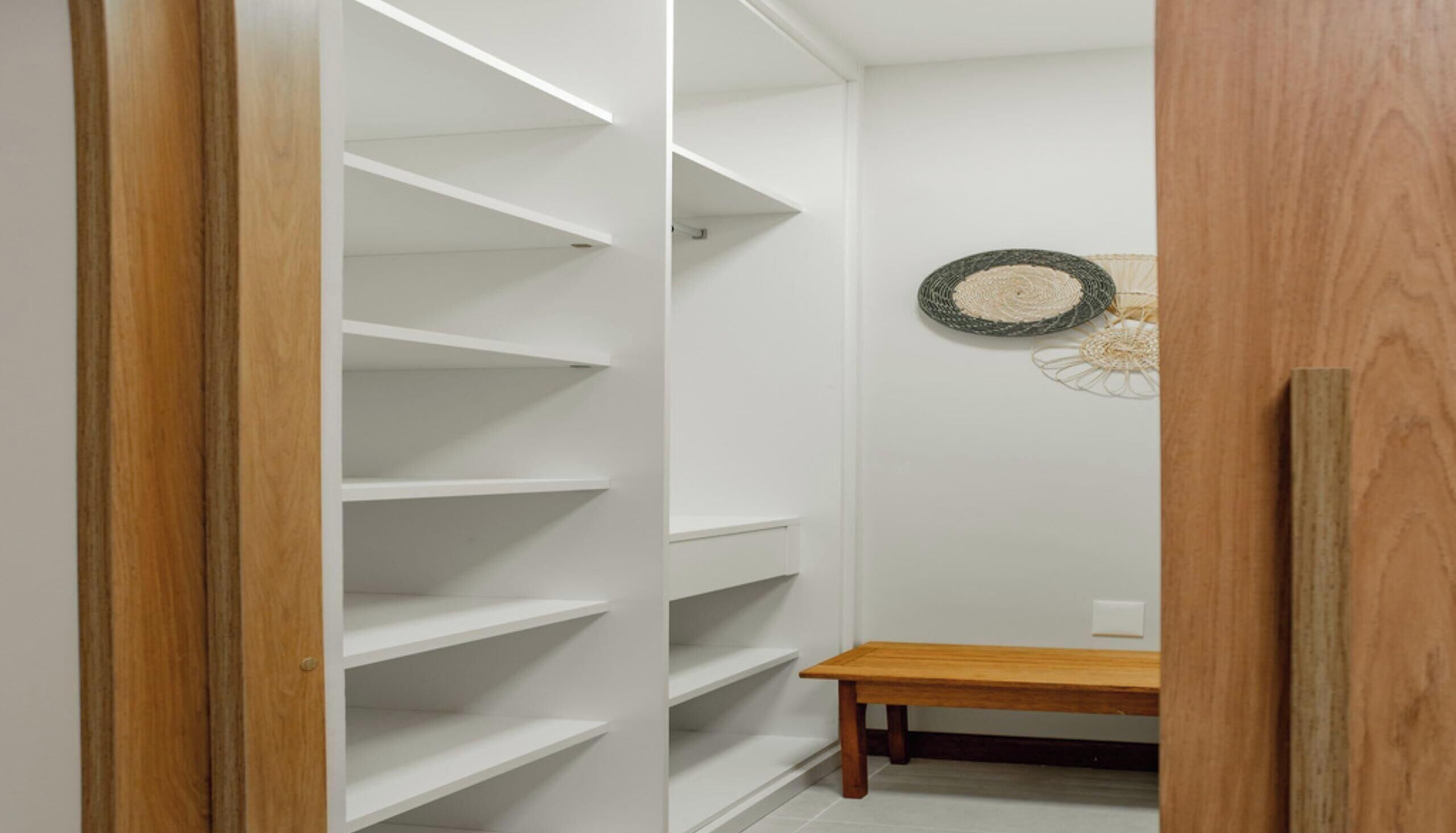 A closet with multiple shelves and a wooden bench.
