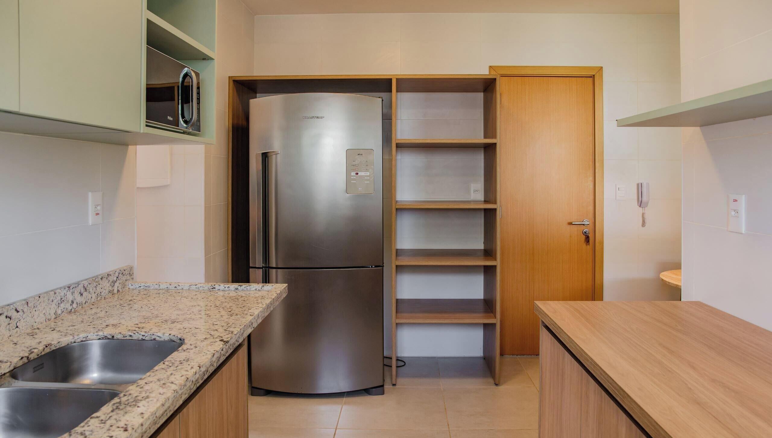 A kitchen with a stainless steel refrigerator, a granite countertop, and wooden cabinets.
