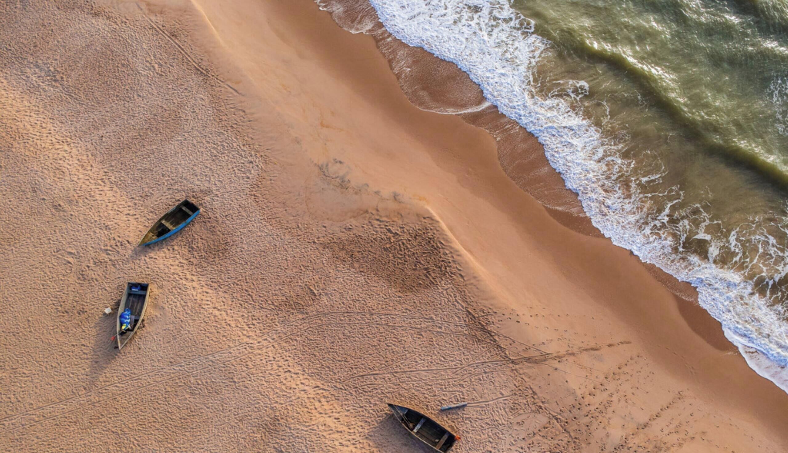 Una playa con tres barcos y una orilla arenosa.