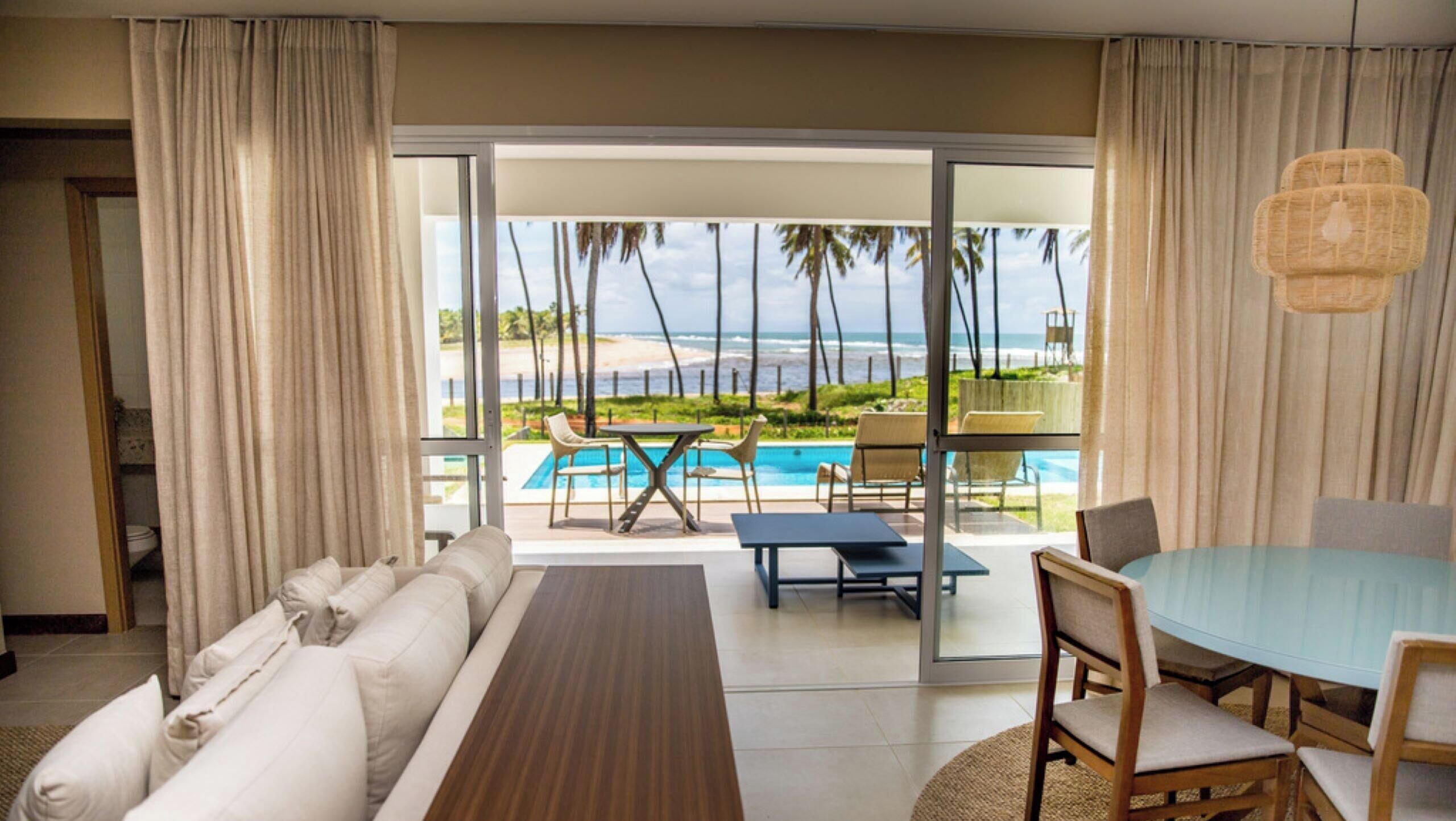Quarto de hotel com sofá, mesa de jantar e vista para a praia e oceano.