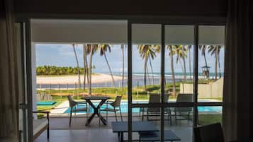 Interior moderno com uma grande porta de vidro deslizante que dá para uma área de piscina com vista para a praia e palmeiras.