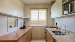 A compact kitchen with a window, a built-in microwave, and a sink. - Ponta de Inhambupe Residences (Esplanada)