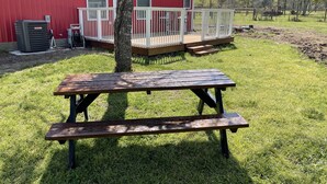 En rød bygning med en hvid veranda, et picnicbord og et træ i en græsplæne.