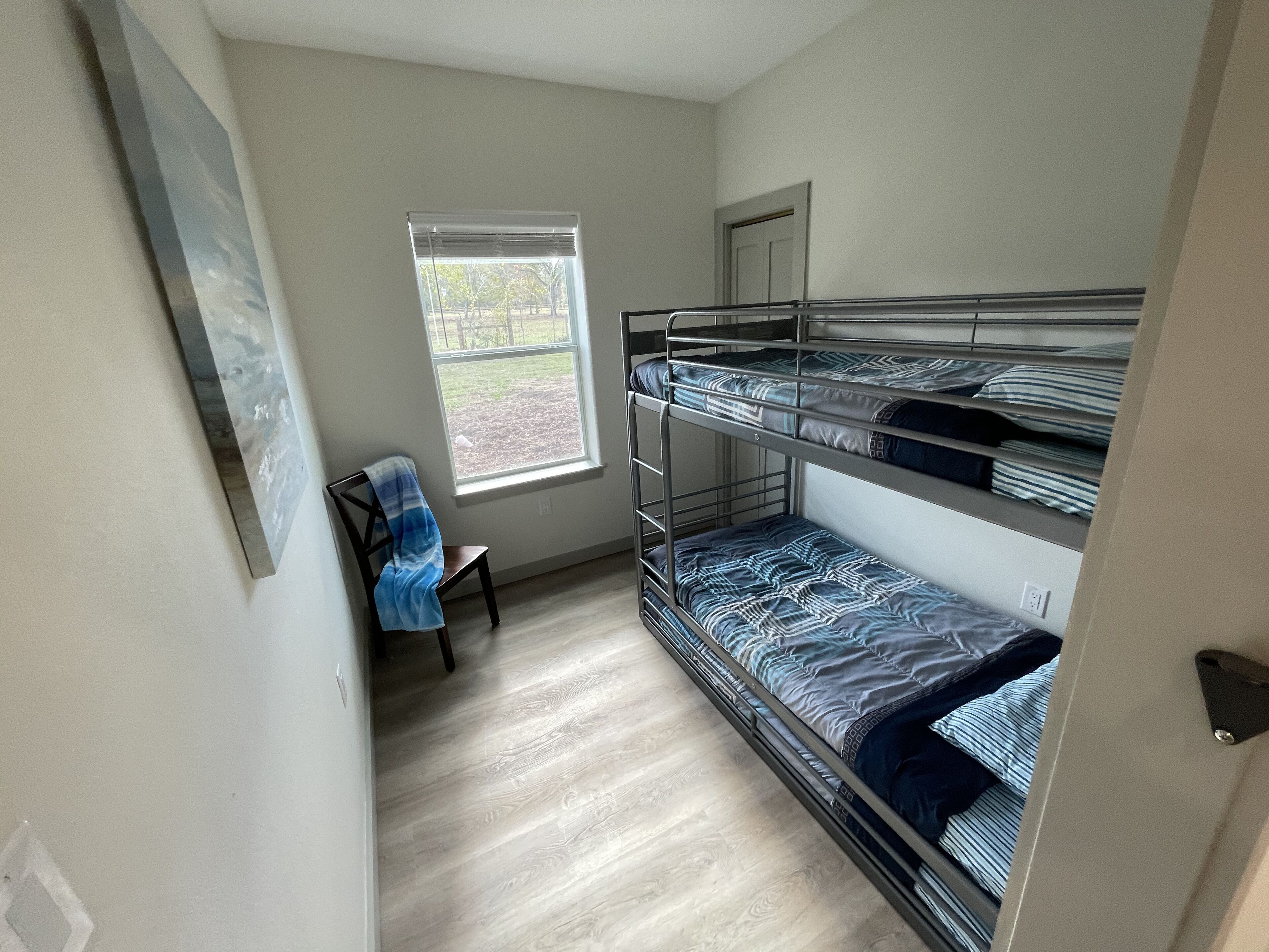 A bunk room with a window, a chair, and a door.