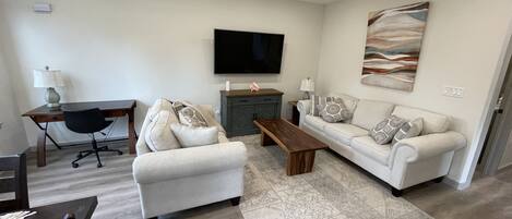 A living room with a sofa, armchair, coffee table, TV, and a ceiling fan.