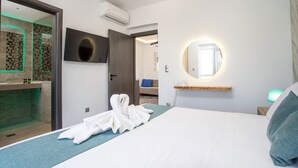A hotel room with a bed, a TV, a mirror, and a bathroom with a glass shower enclosure. - Platoni Elite Luxury apartment (Ιαλυσός)