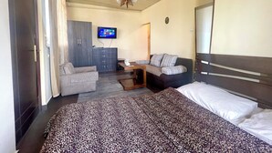A hotel room with a bed, a sofa, a TV, a wardrobe, and a desk.